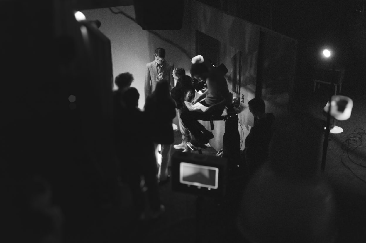Film crew working around actors and camera on a dark set